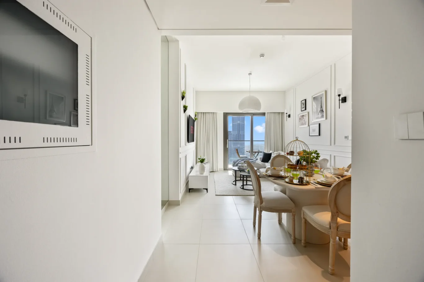 Bright open-plan living and dining area in a white modern apartment, with a round dining table and city skyline visible through the window