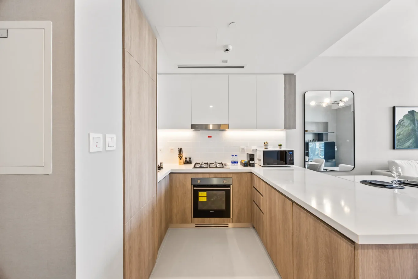 Modern kitchen with white upper cabinets, wood lower cabinets, an island, gas cooktop, oven, microwave, and a large wall mirror.