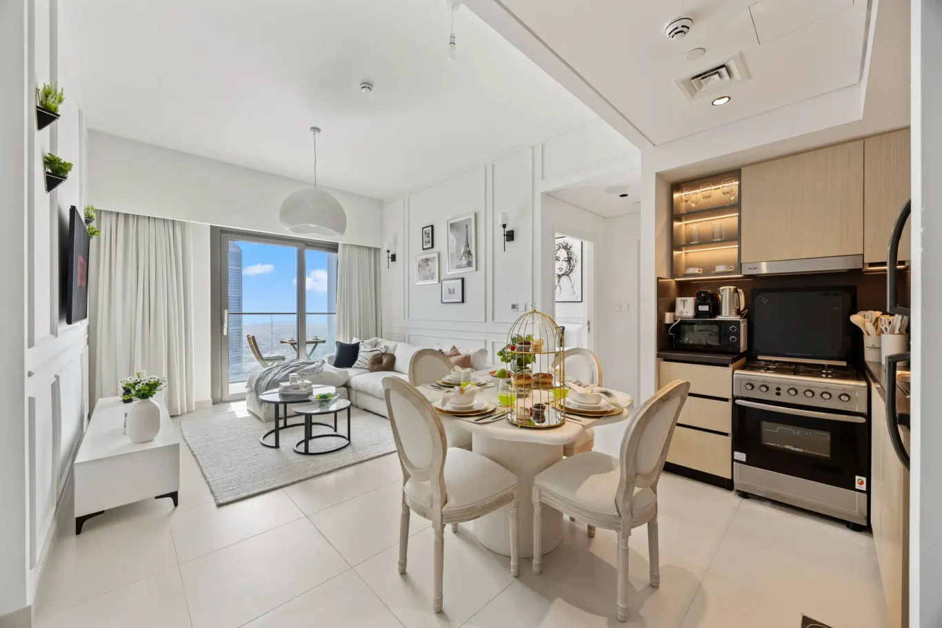 Bright open-plan living and dining area in white tones with a city skyline view, a four-seat dining table, and a modern kitchen.