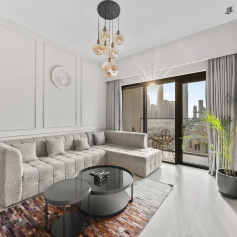 Modern living room with a beige sectional sofa, round black coffee tables, and a wall-mounted Netflix TV near a balcony with a city view.