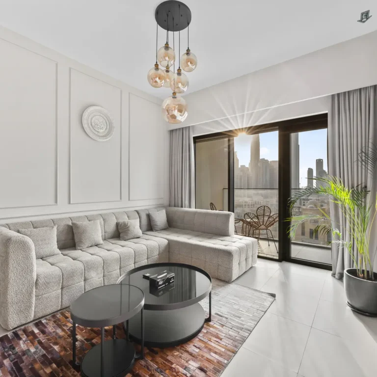 Modern living room with a beige sectional sofa, round black coffee tables, and a wall-mounted Netflix TV near a balcony with a city view.