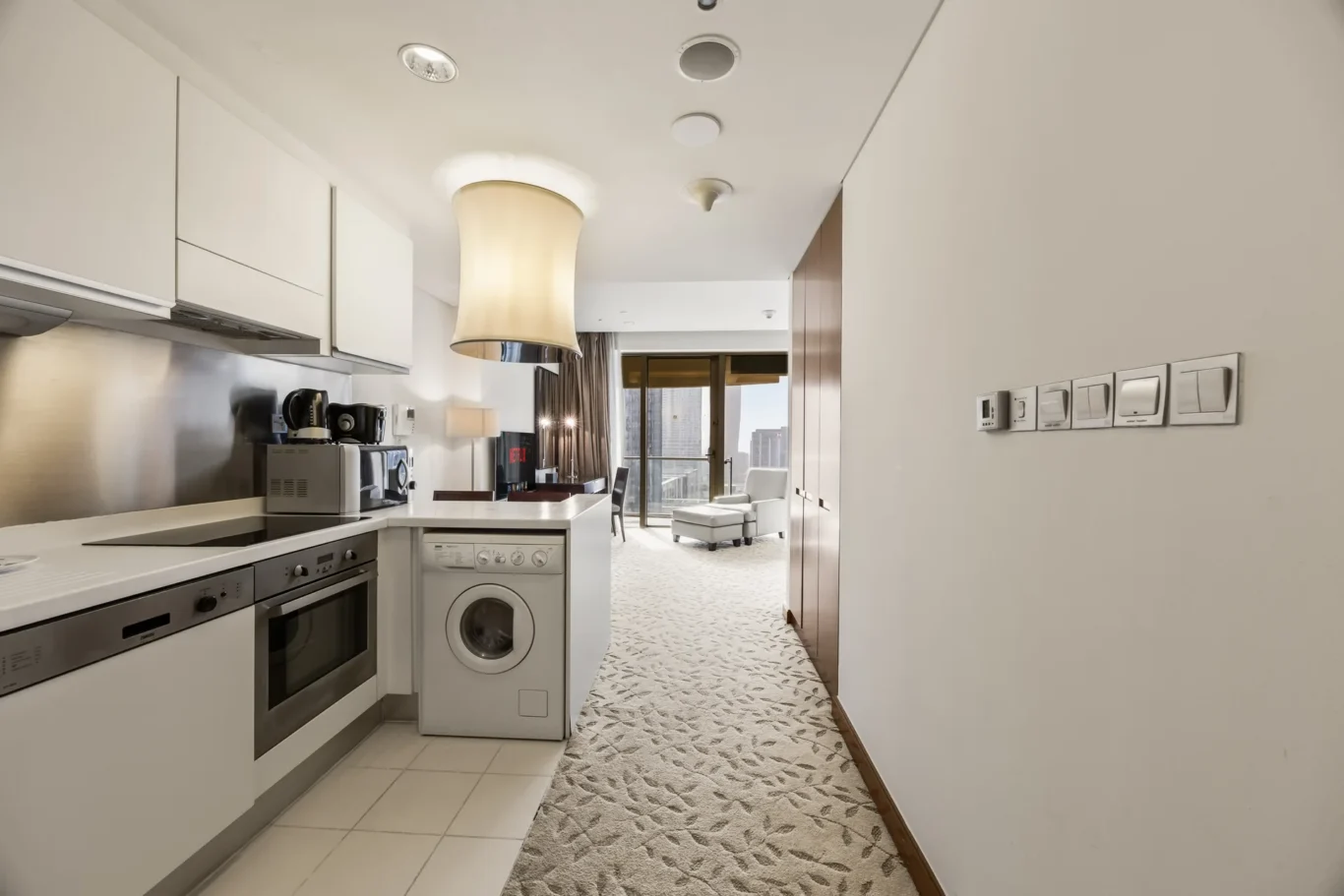 Modern white kitchen with stainless steel oven, dishwasher, washing machine, microwave, and kettle on the counter.