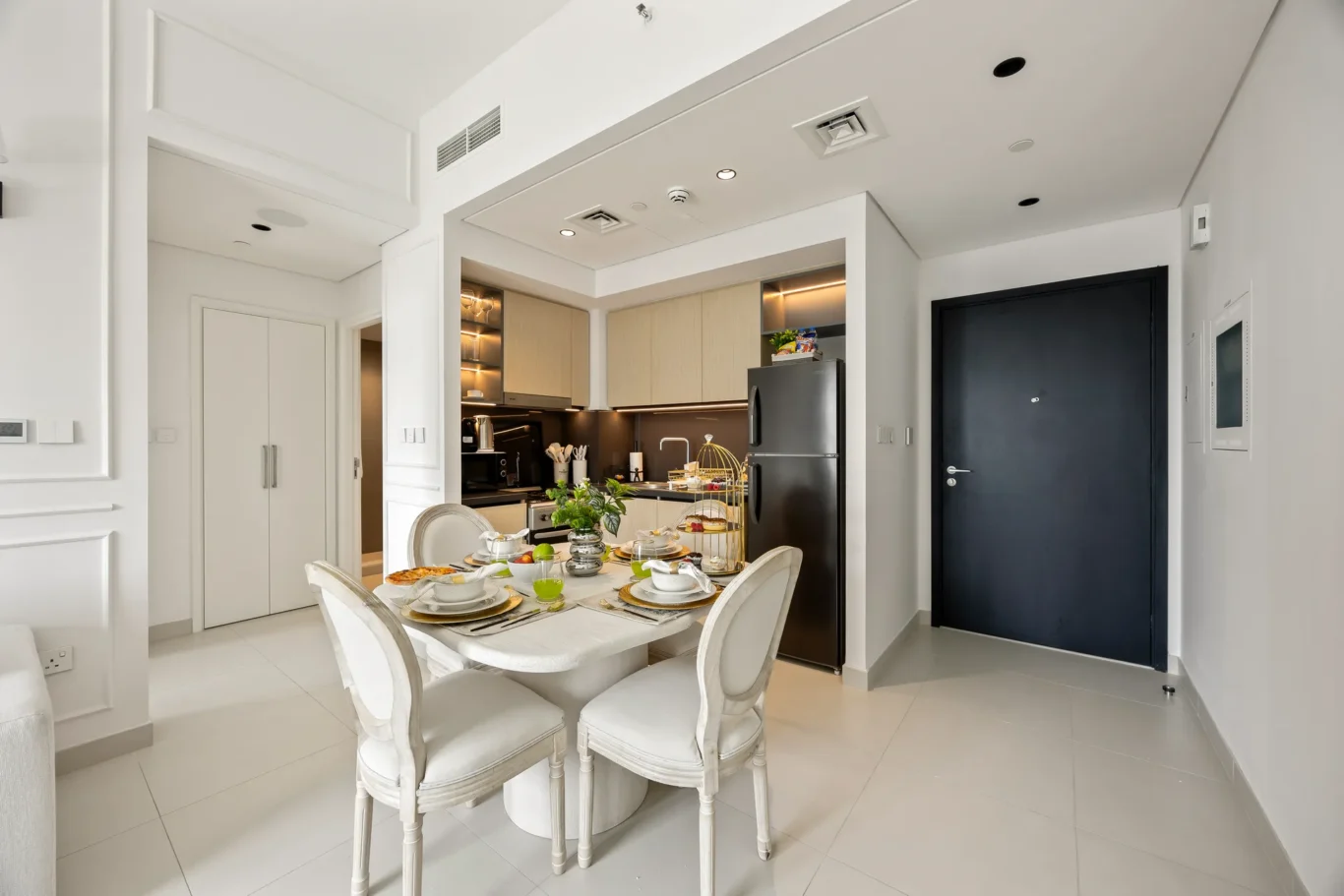 Bright dining area with a white marble table set for six, adjacent to a modern kitchen with stainless steel appliances.