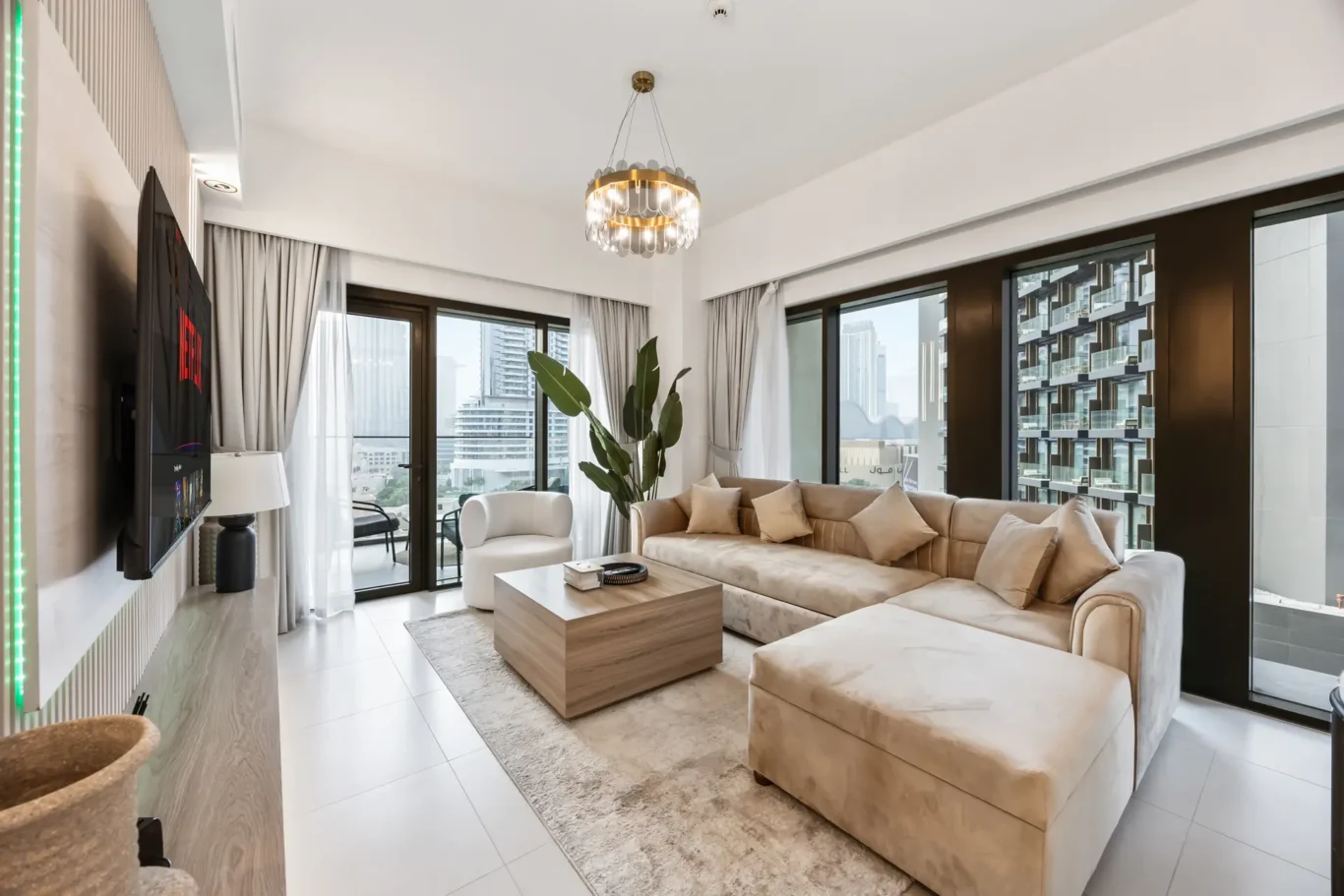 Modern living room with a beige sectional sofa, glass coffee table, and city-view windows.