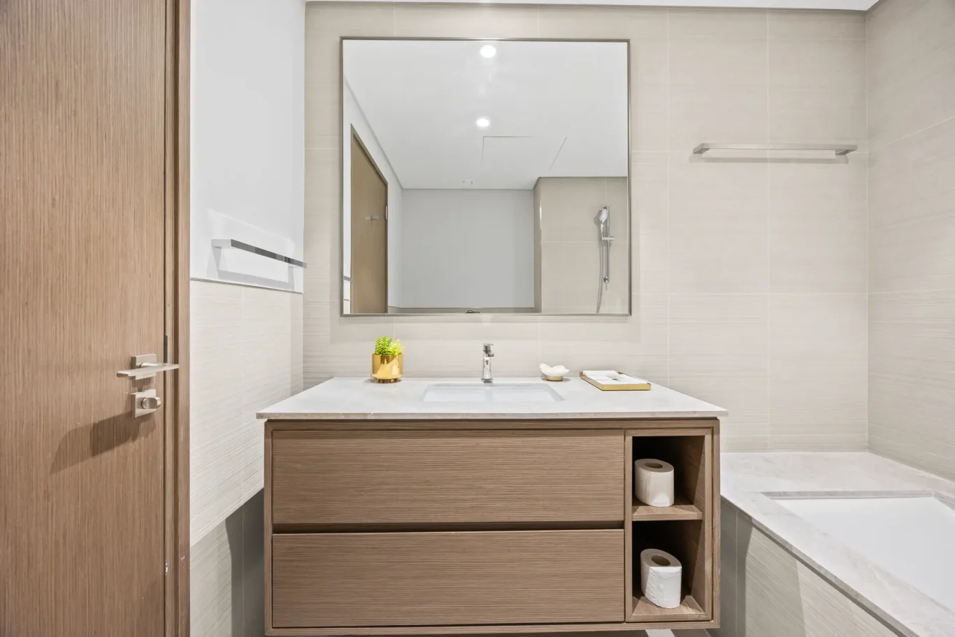 Modern bathroom with a wooden vanity, marble countertop, and large mirror; towel rail on beige tiled wall.