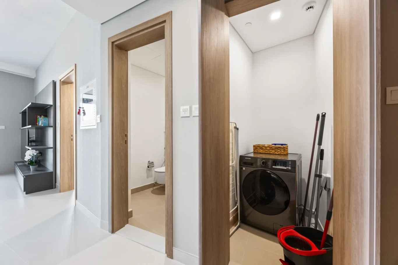 Bright hallway with a wooden doorway to a bathroom on the left and a laundry area with a front-load washer on the right.