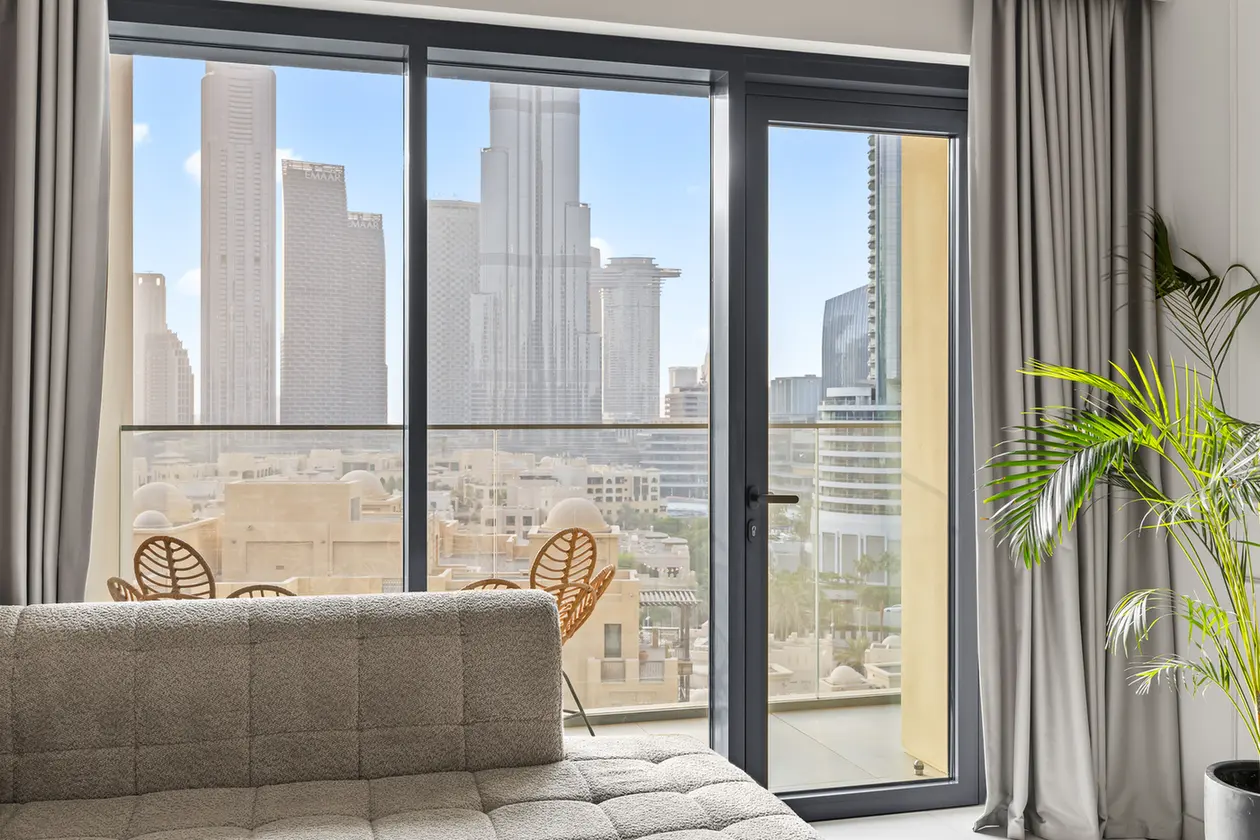 Living room with a gray sectional facing glass doors leading to a balcony and a city skyline beyond the windows.
