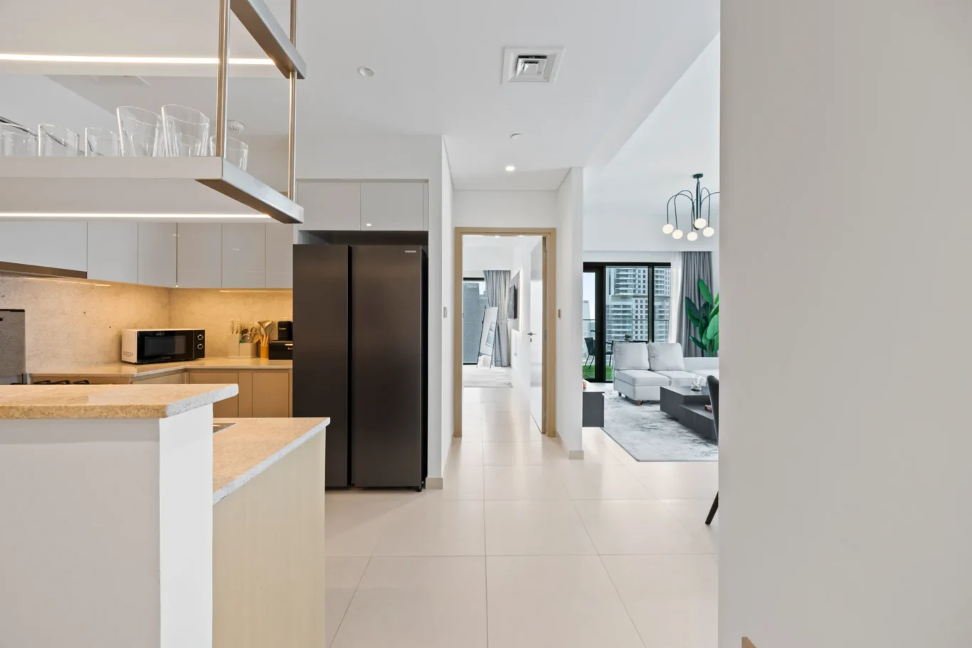 Open-concept kitchen with white cabinets, island, and a black-side-by-side refrigerator, leading to a living area with large windows and city views.