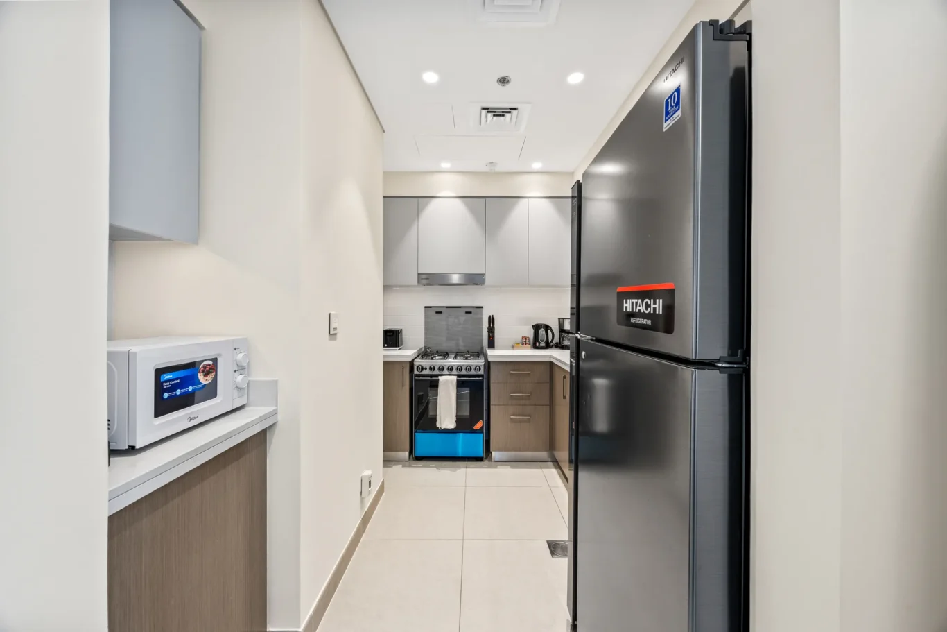Narrow modern kitchen with stainless refrigerator on the right and white cabinets along the back wall.