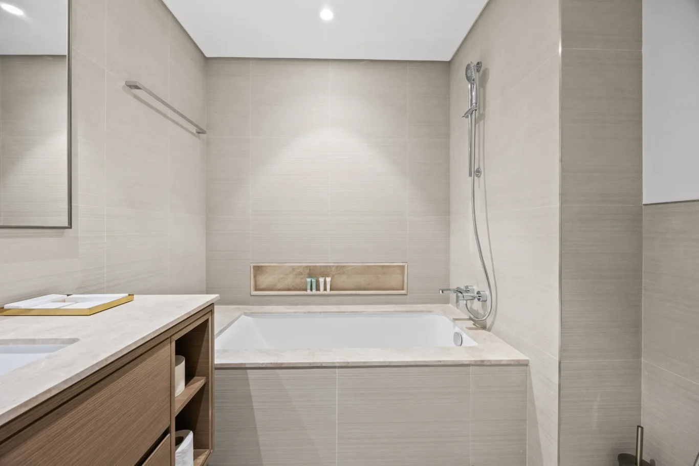 Modern beige tiled bathroom with built-in tub, wall-mounted shower, and wooden vanity.