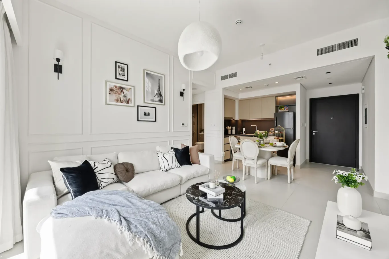 Bright open-plan living room with a white sofa, cushions, and a round black marble coffee table on a light rug