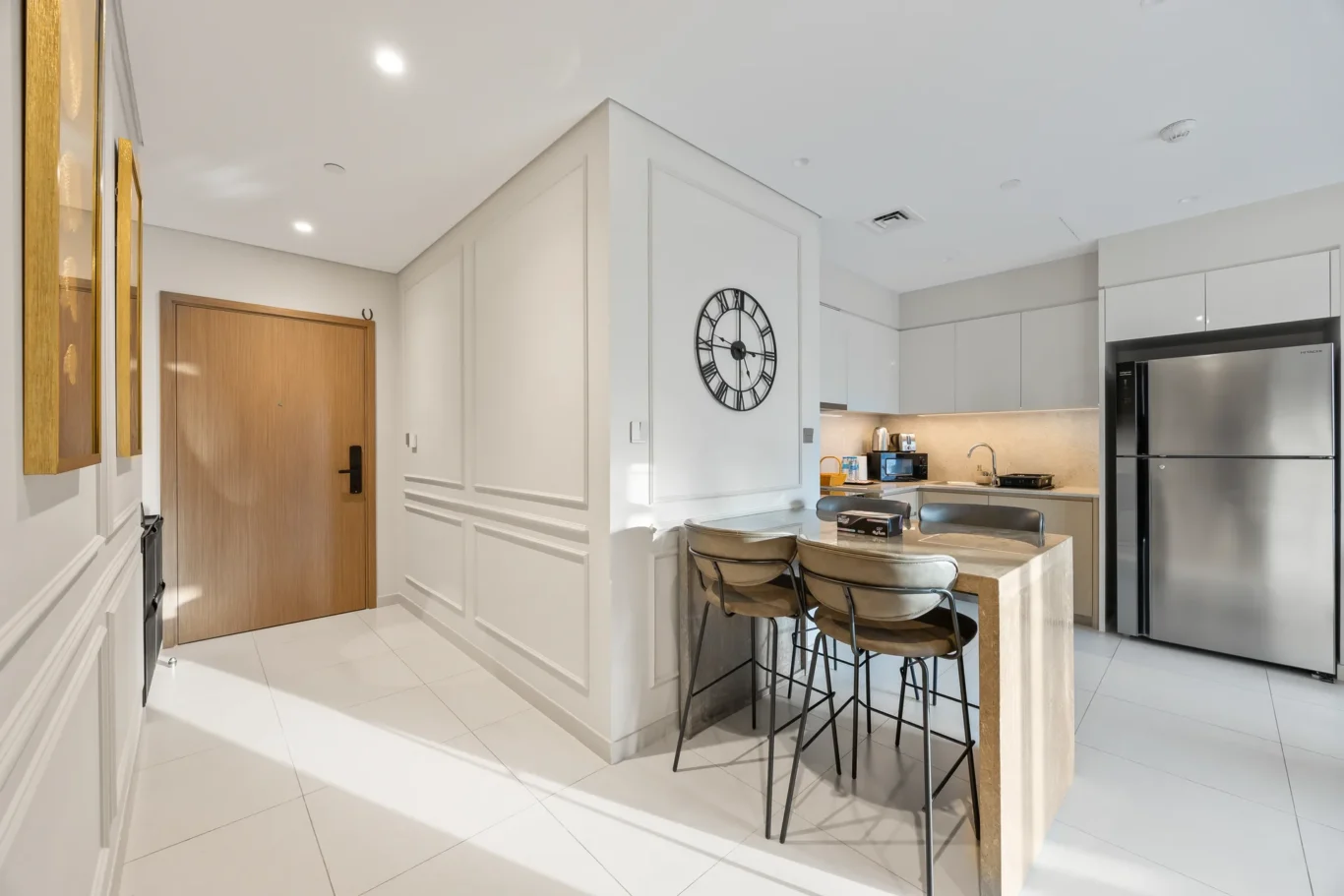 Modern kitchen with white cabinets, a breakfast island with four metal-and-leather stools, and a stainless fridge nearby.