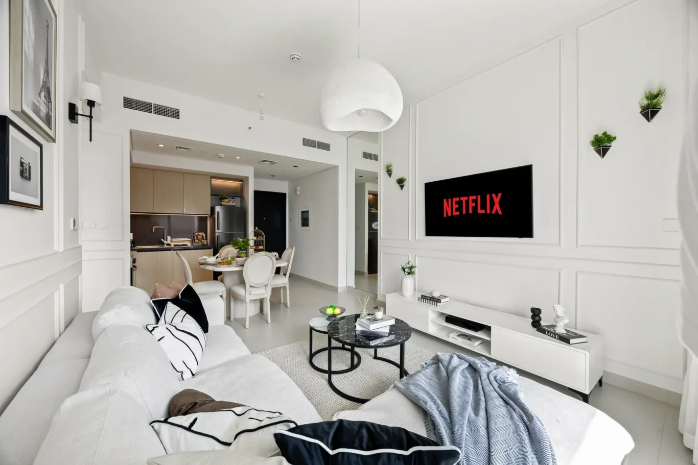 Bright, modern living room with white walls, a wall-mounted Netflix screen, and a white sofa facing the TV.