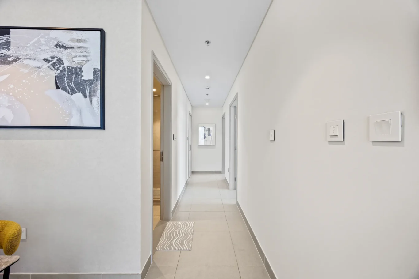 Bright modern hallway with gray walls, a framed abstract painting on the left, and light switches on the right wall near the foreground.