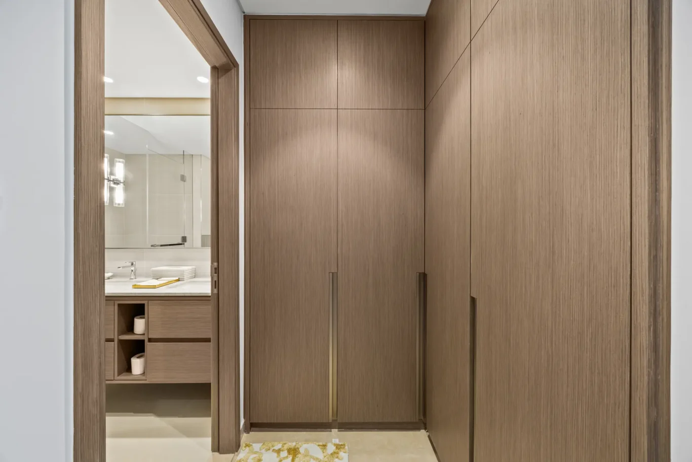 Tall wooden cabinets line a narrow hallway; bathroom visible through an open door on the left.
