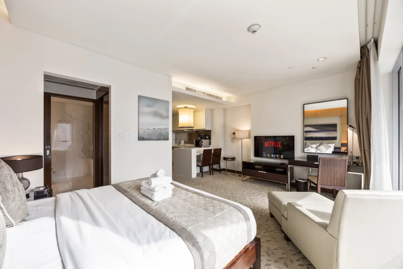 Hotel suite: two neatly made beds with towels, seating area, and a Netflix-enabled TV in view of a spacious room.