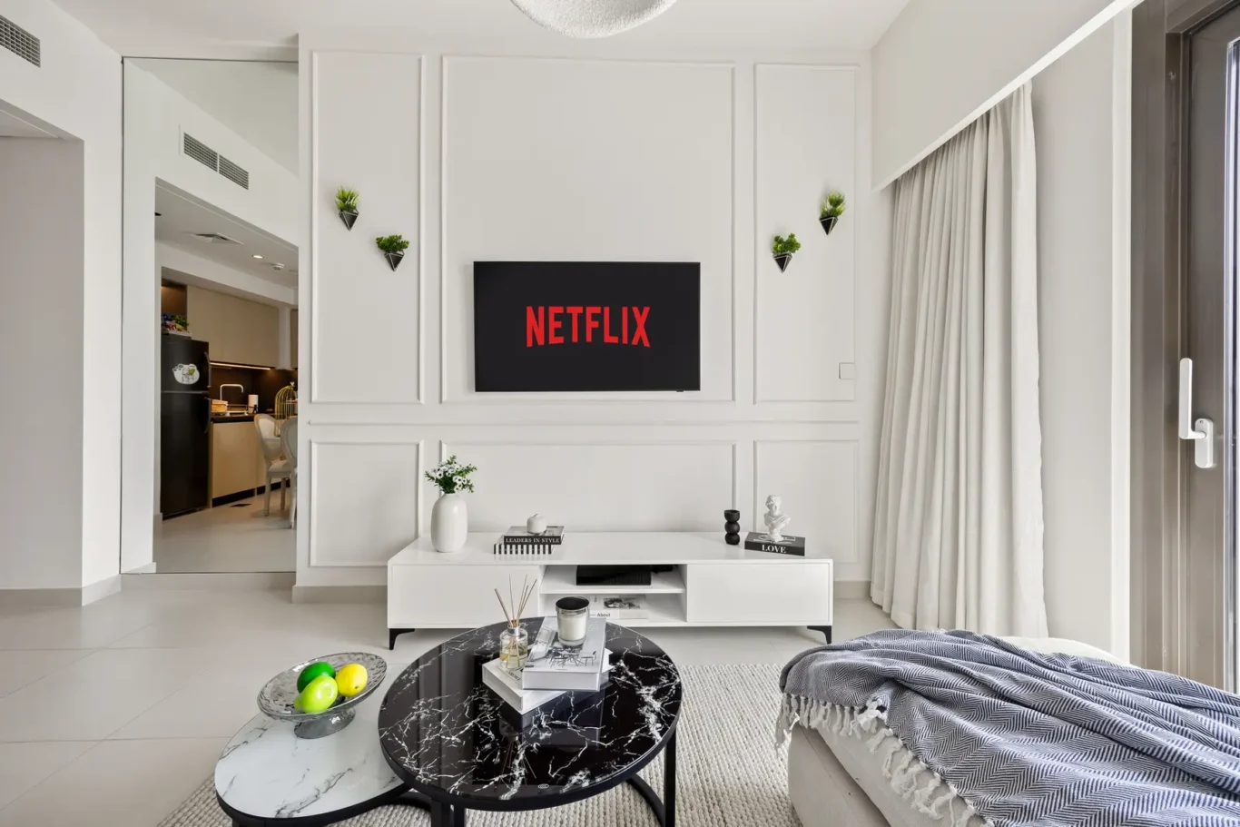 Minimalist living room with a wall-mounted Netflix screen centered on a white paneled wall, flanked by small wall planters.