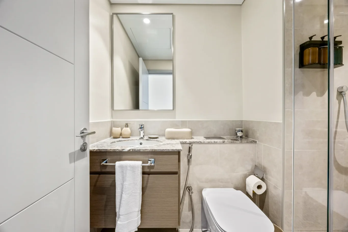 Modern bathroom with wooden vanity, marble countertop, porcelain sink, and large mirror above it.