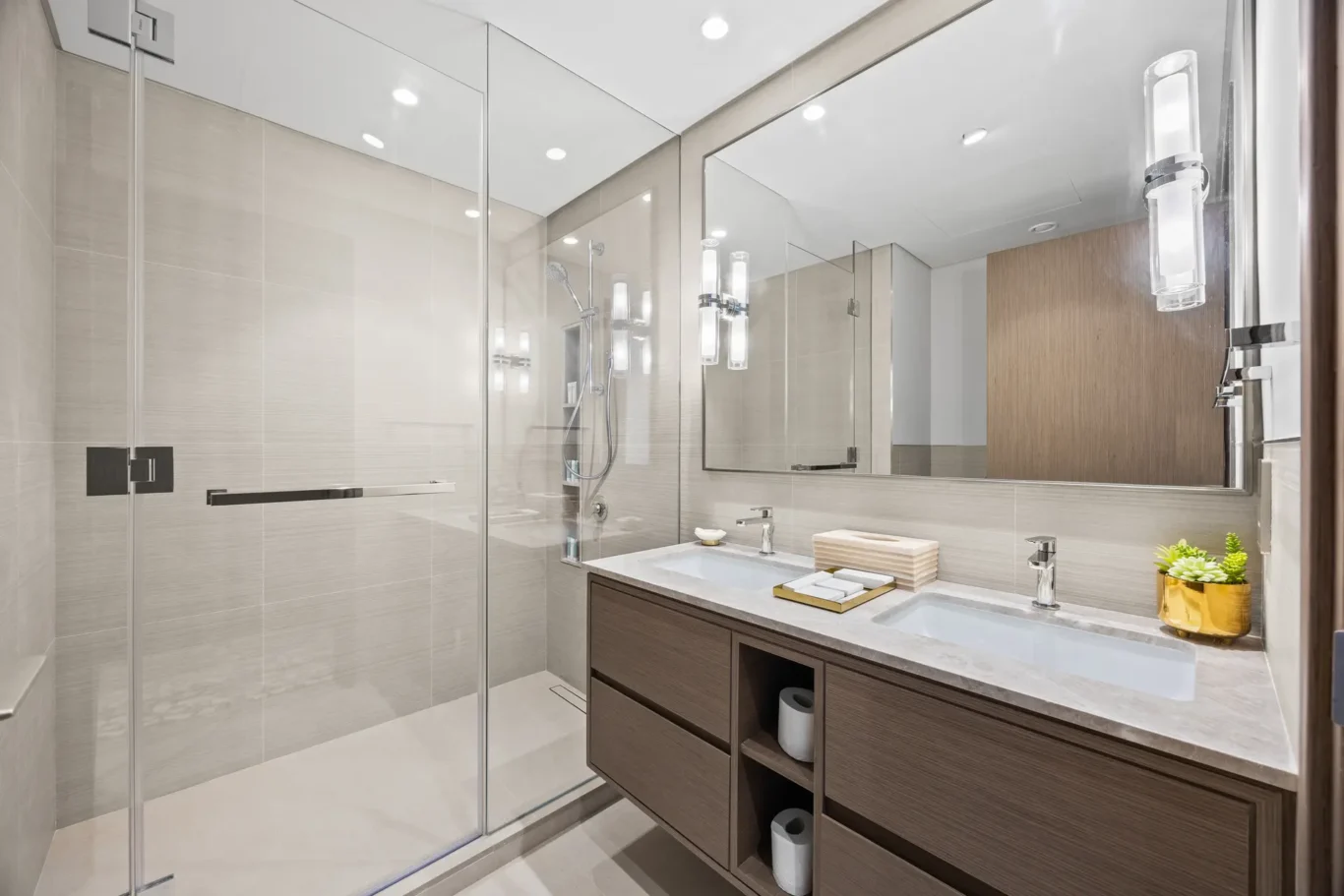 Modern bathroom with glass shower enclosure, double sink vanity, and beige tiled walls.