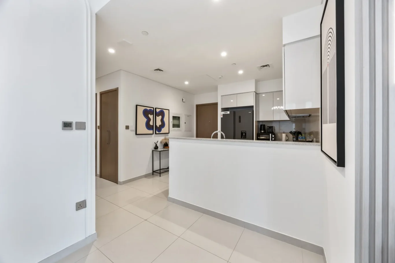 Bright modern kitchen with white cabinets, gray countertop island, and stainless steel refrigerator; blue abstract art on the wall.