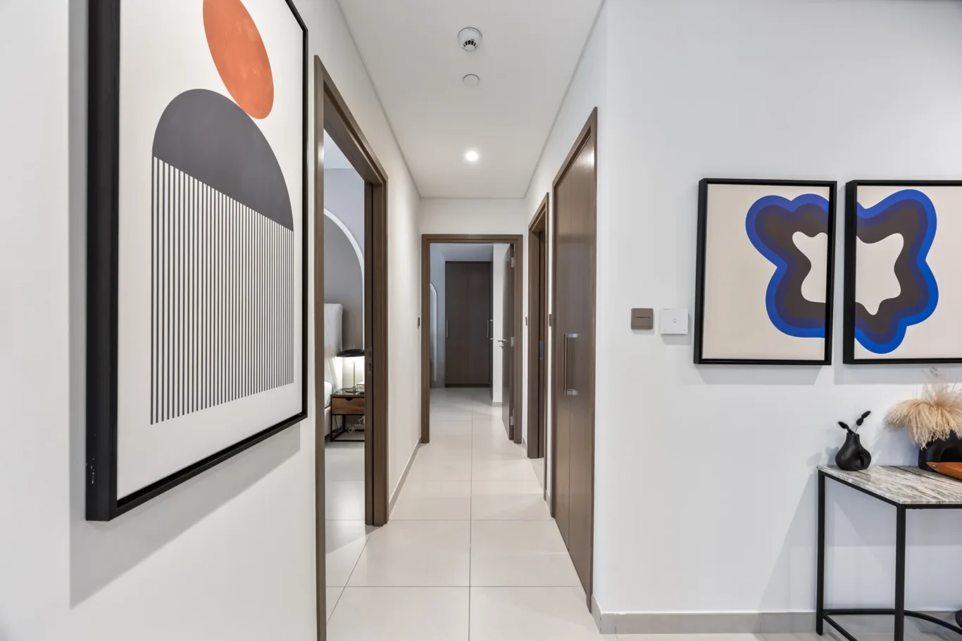 Bright hallway with white walls, wooden doors, and large abstract framed artwork along the walls.