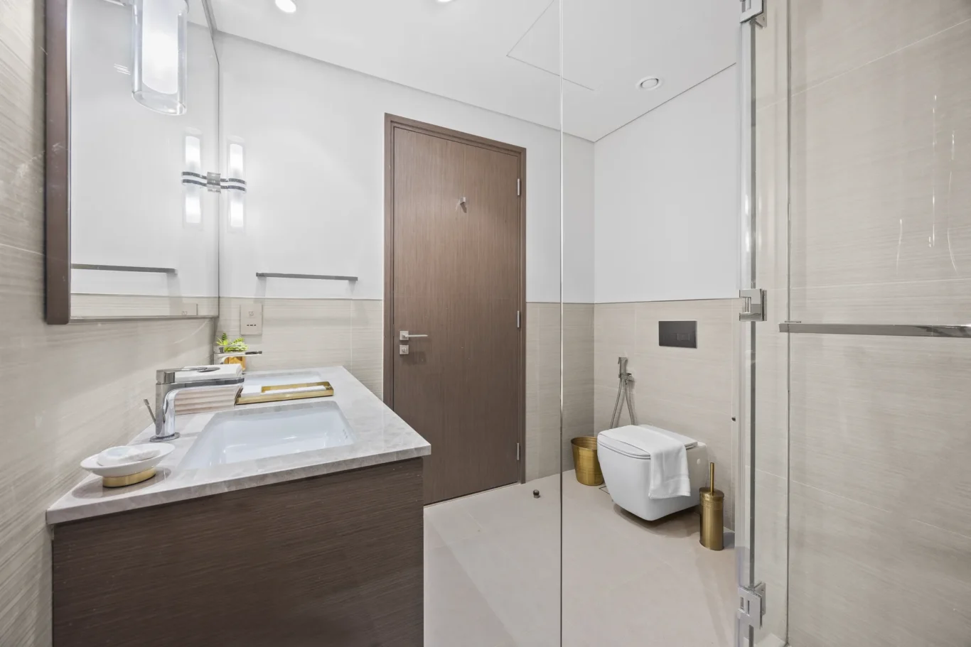 Modern bathroom with double sinks, wood vanity, large mirror, glass shower, and wall-mounted toilet.