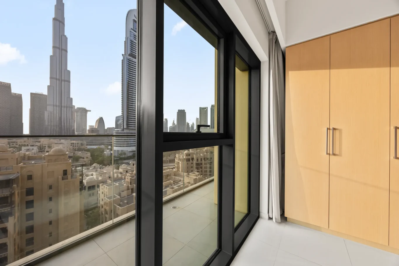 Interior room with large black-framed glass window looking out to a city skyline; light wood cabinets on the right.