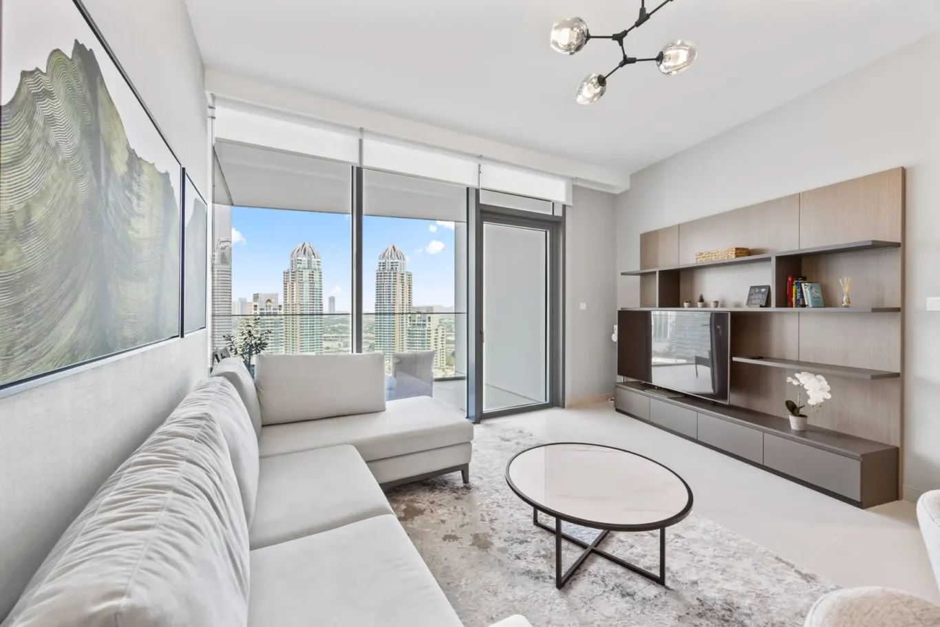 Contemporary living room with a gray sectional, round coffee tables, and a TV wall, plus a city view through large windows.