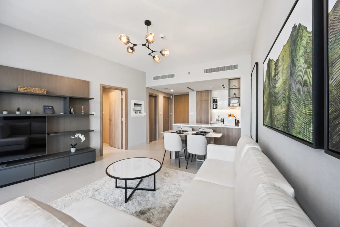 Open-plan living and dining area with a cream sectional, round marble coffee table, gray shelving, and a dining table near the open kitchen.