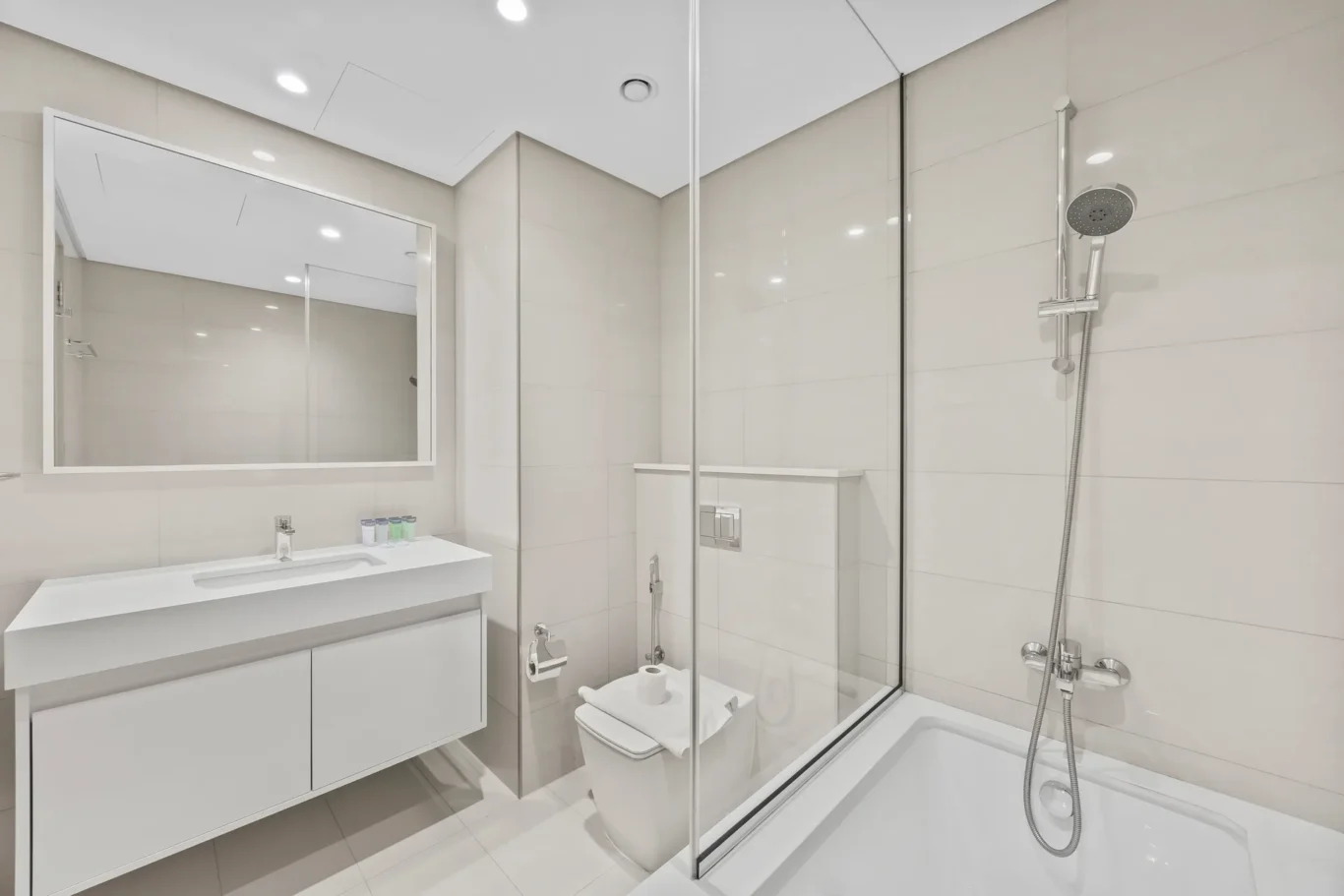 Modern minimalist bathroom with a floating vanity, large mirror, and glass shower enclosure surrounded by white tiles.