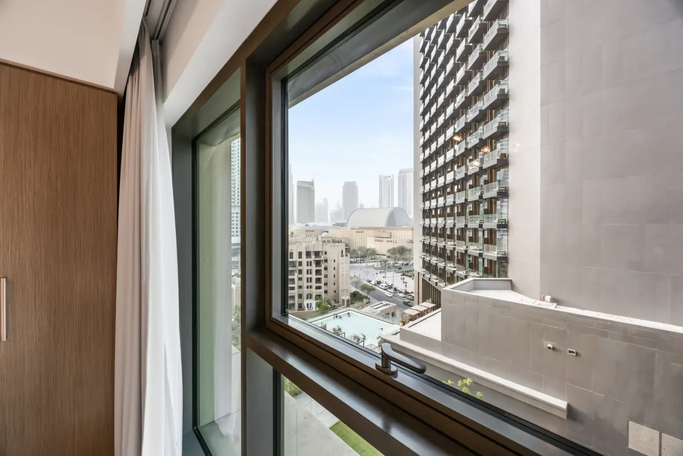 Hotel room window with a cityscape view of high-rise buildings and a pool below.