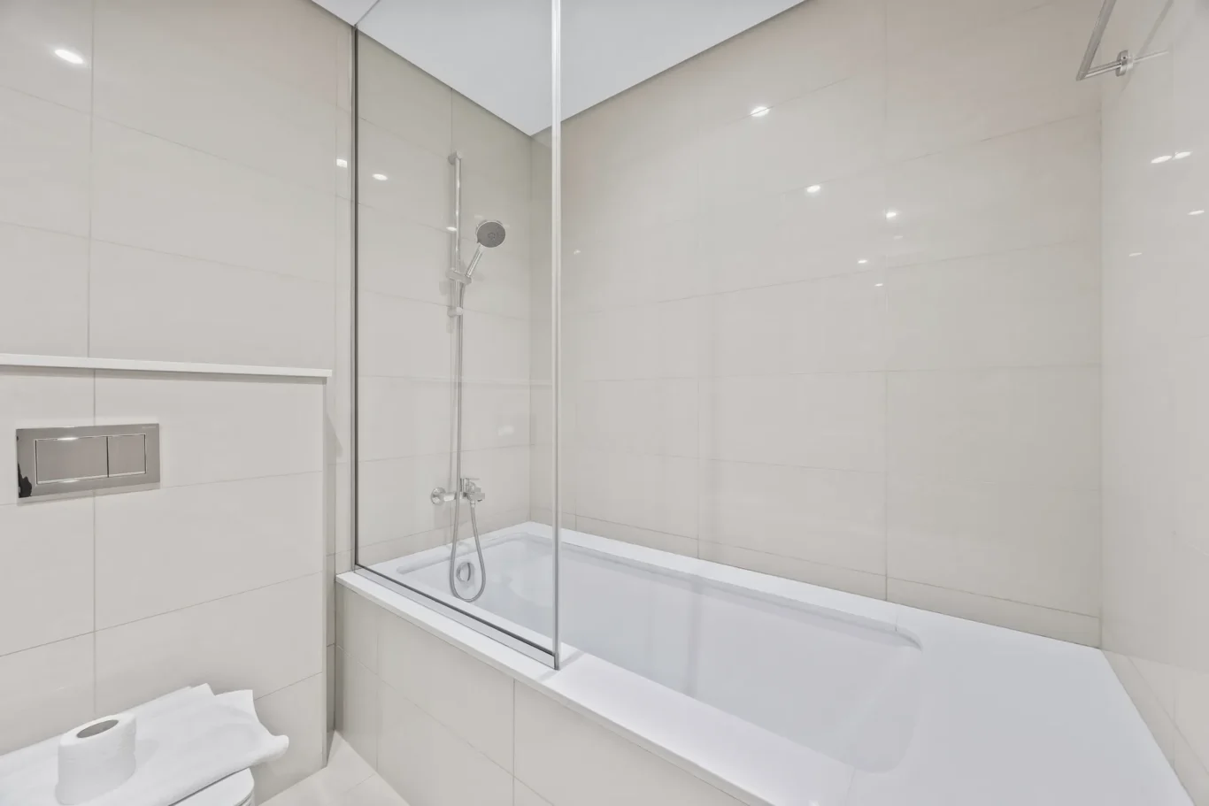 Minimalist bathroom with a built-in white bathtub, glass shower screen, and glossy white tiles.