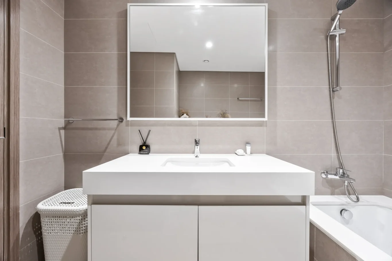 Modern bathroom with white vanity and large mirror, shower to the right and a bathtub at the edge.