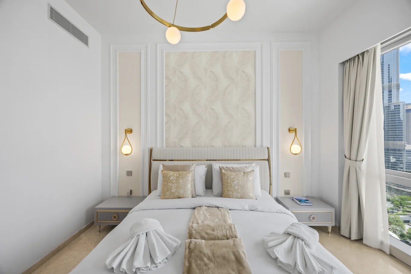 Luxurious hotel-style bedroom with a padded headboard, cream and gold accents, two side tables, and decorative wall panels flanking a large central panel behind the bed.