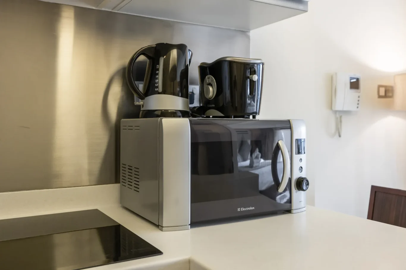 Stainless steel kitchen counter with a silver Electrolux microwave; a black kettle and a black toaster sit on top of the microwave.
