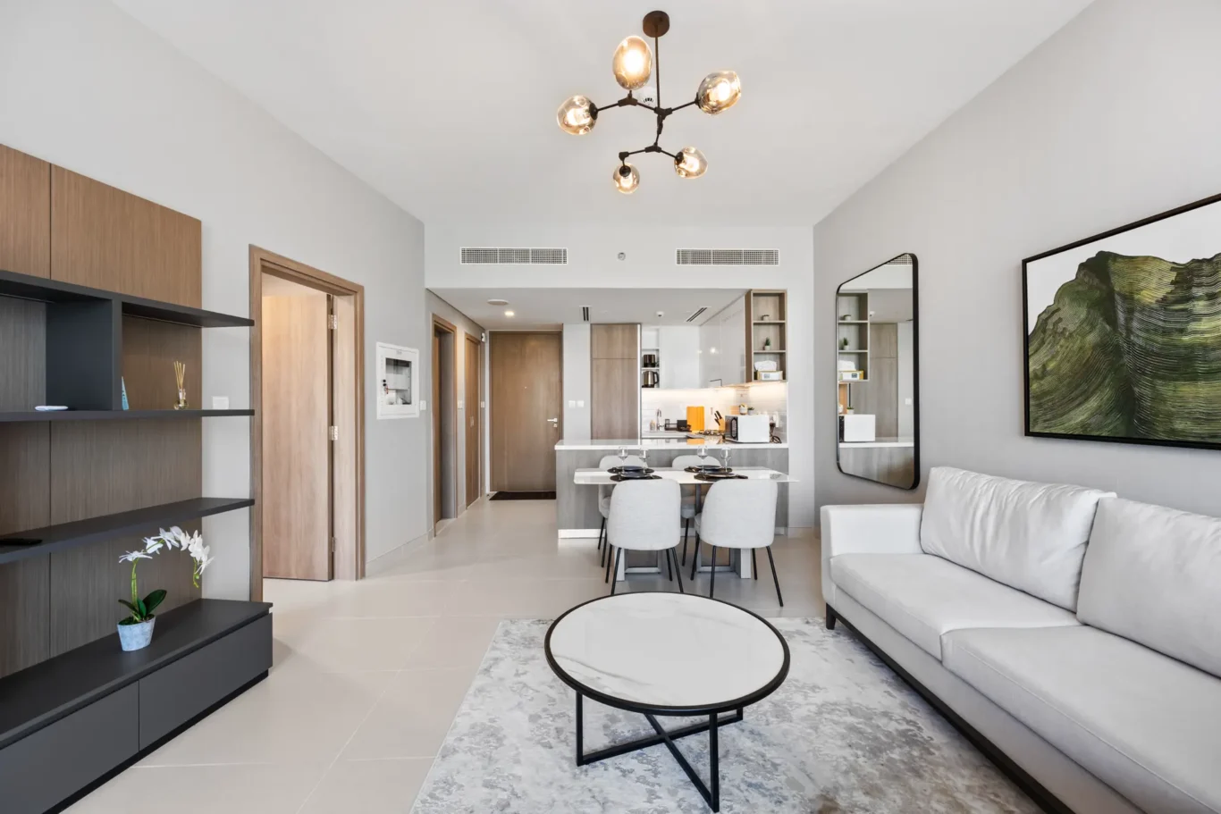 Modern open-plan living room with a gray sofa, round marble coffee table, and a large wall art piece; dining area and kitchen visible in background.