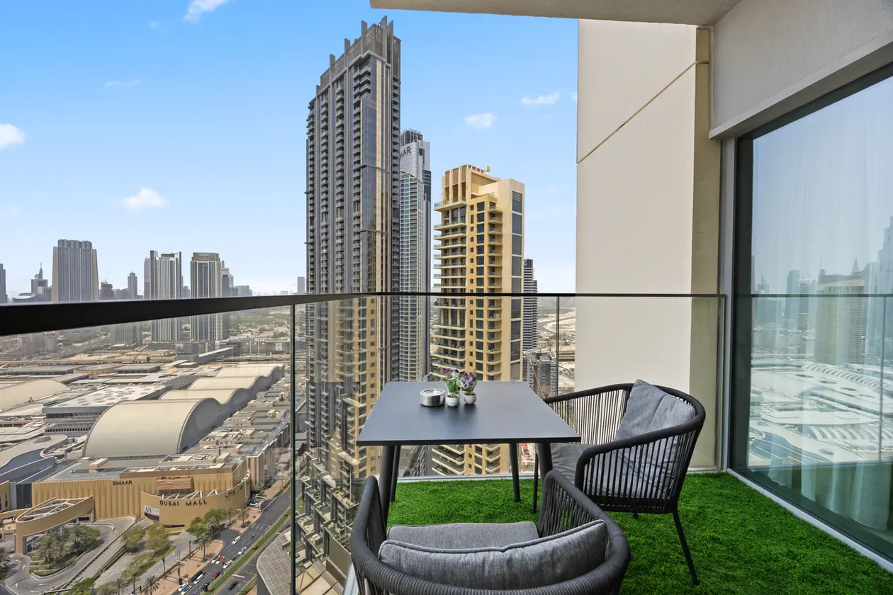 Balcony seating on a high-rise terrace with a dark table and gray cushions, overlooking a canyon of tall skyscrapers under a blue sky.
