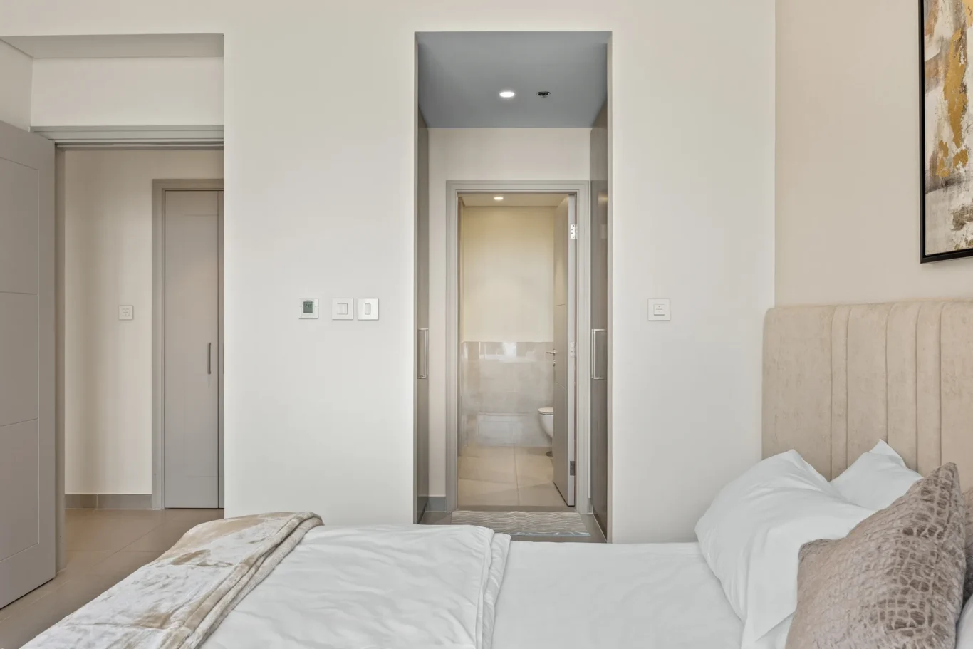 Hotel bedroom with white walls, plush bed, and doorway leading to a tiled bathroom.