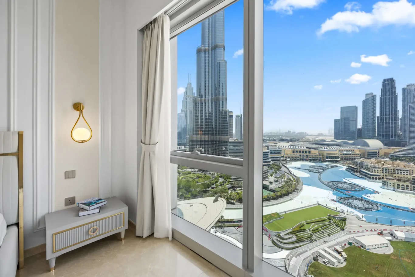Luxurious hotel room corner with white and gold furniture and a large window overlooking a modern city skyline.