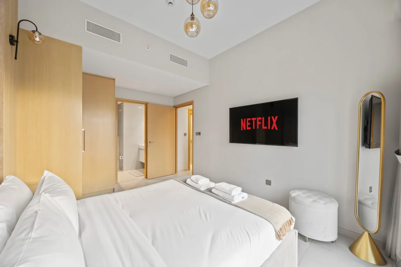Hotel room with two white beds, wall TV showing Netflix, and wooden doors in a bright, modern space to relax or sleep in.