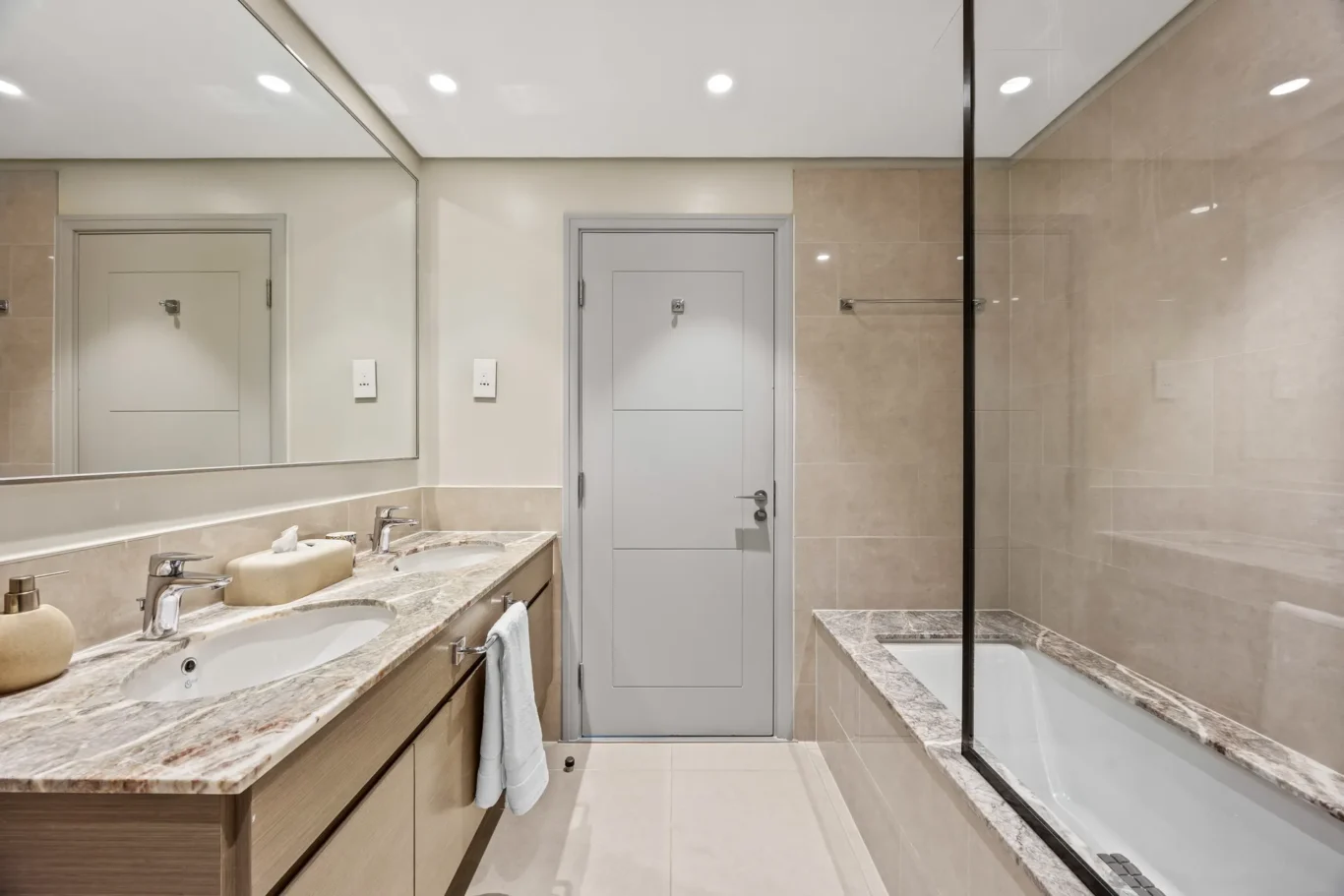 Contemporary bathroom with dual sinks, marble countertop, large mirror, and a glass-enclosed shower on the right.
