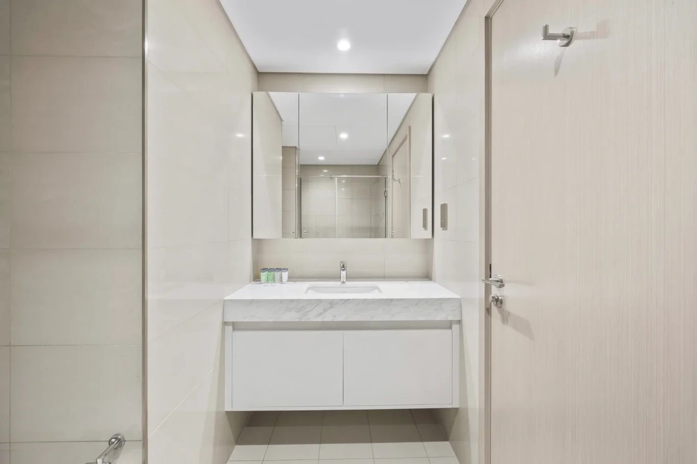 Modern white bathroom vanity with marble countertop and large mirrored medicine cabinet, small toiletries lined up beside the sink.
