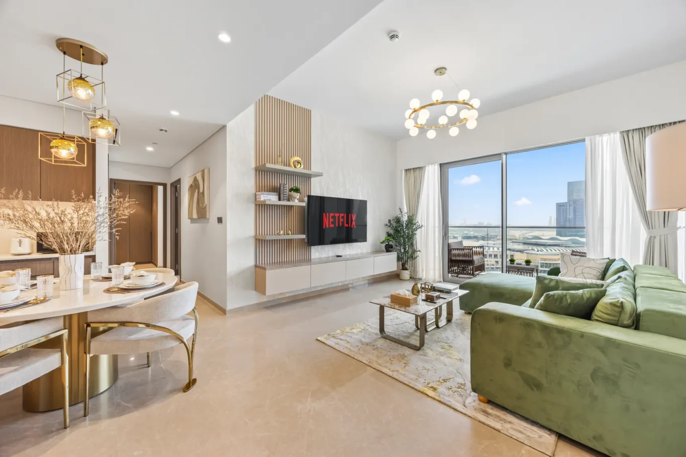 Open-plan living and dining area with a green sofa facing a wall-mounted Netflix TV, gold accents, and large city-view windows.