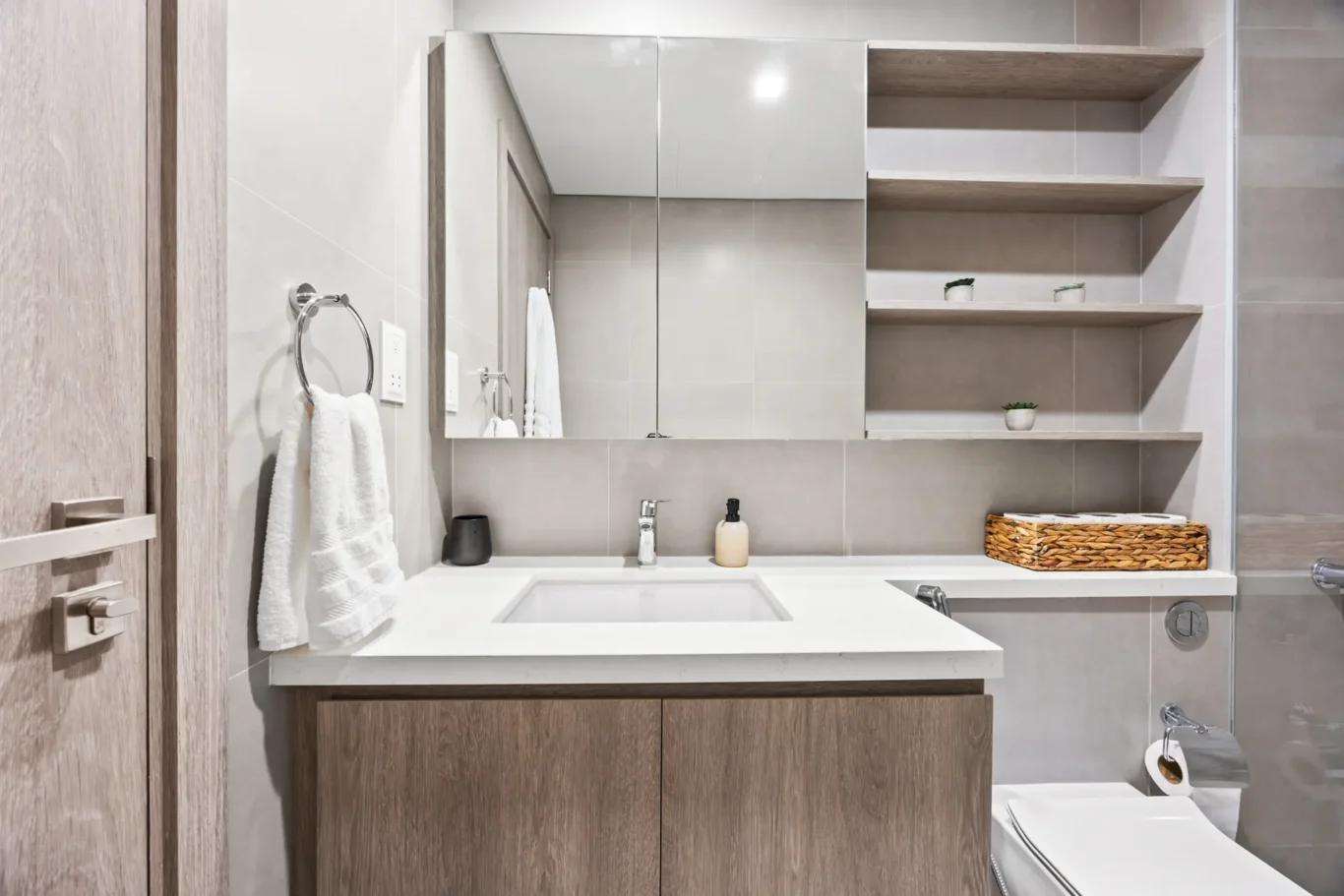 Modern bathroom vanity with white countertop, sink, chrome faucet, and open wooden shelves with small plants.