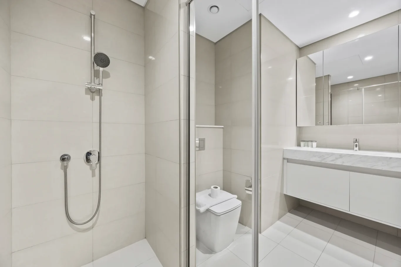 Modern bathroom with a glass shower enclosure, wall-mounted showerhead, and a white toilet beside a marble vanity.
