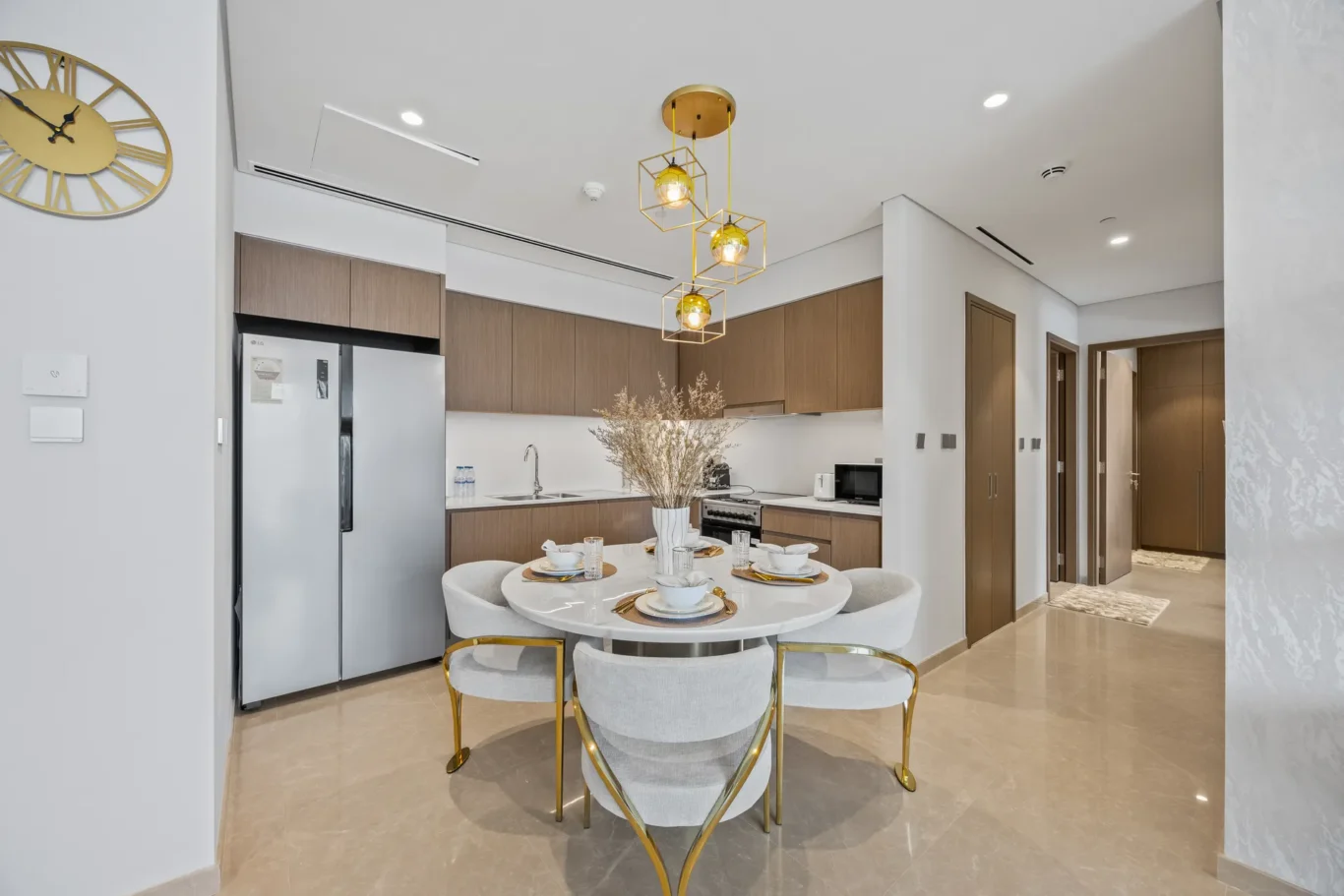 Open-plan kitchen and dining area with a round dining table set for four, beige chairs, and a gold geometric pendant light fixture above.