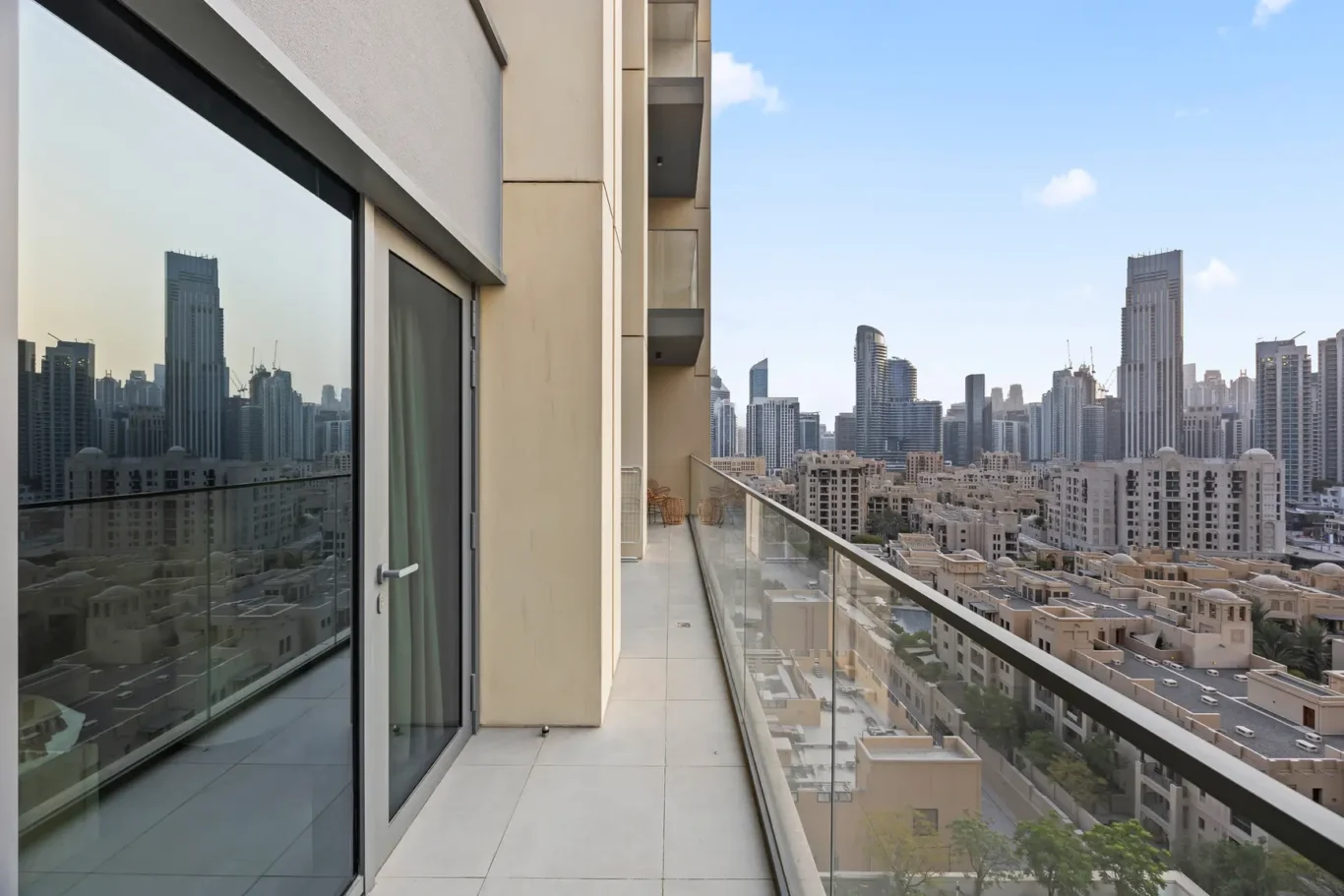Balcony of a high-rise apartment with glass railing, overlooking a dense city skyline of modern skyscrapers under a clear blue sky