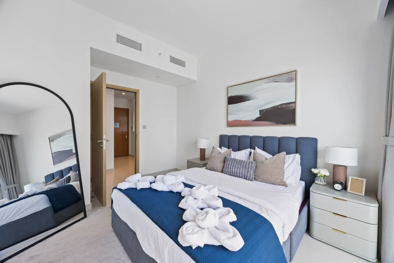 Hotel bedroom with a blue upholstered headboard, white bedding, and folded towels arranged on the bed.