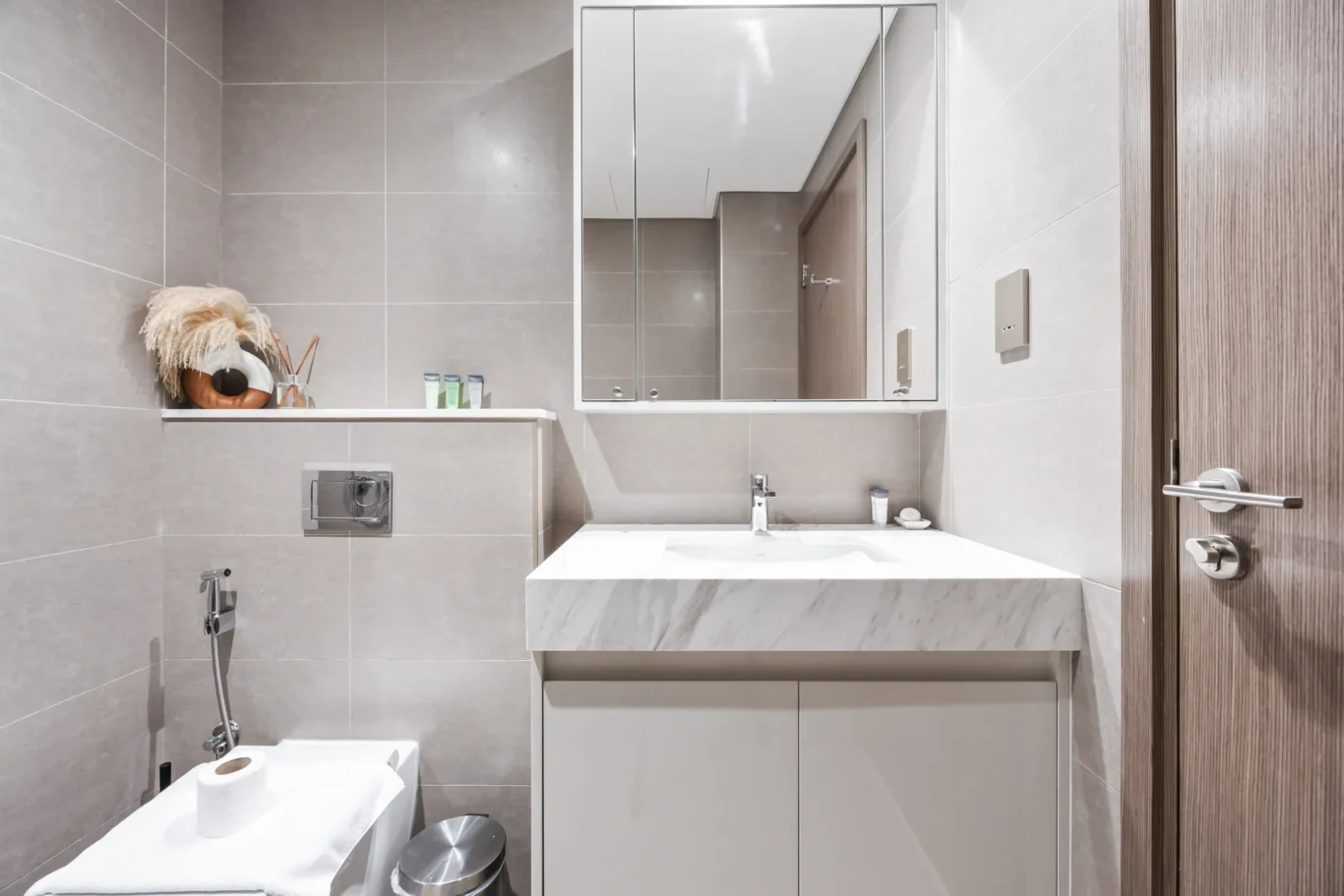 Modern bathroom with gray tile walls, white vanity, and a large mirrored cabinet above the sink.