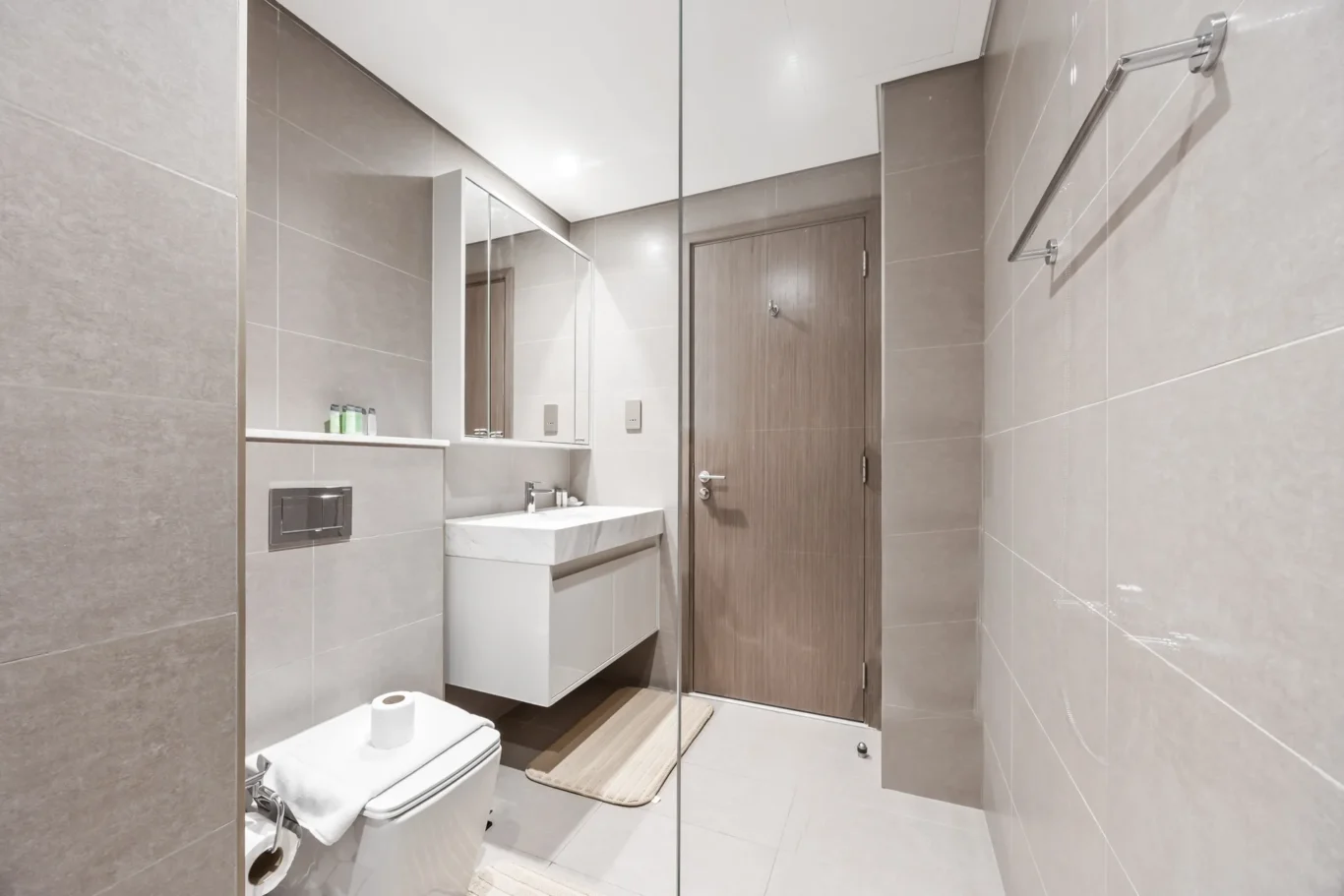 Modern bathroom with a glass shower enclosure, white vanity and wall-hung toilet in neutral tones.